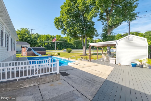 view of pool featuring a water slide, a shed, a yard, a wooden deck, and a patio