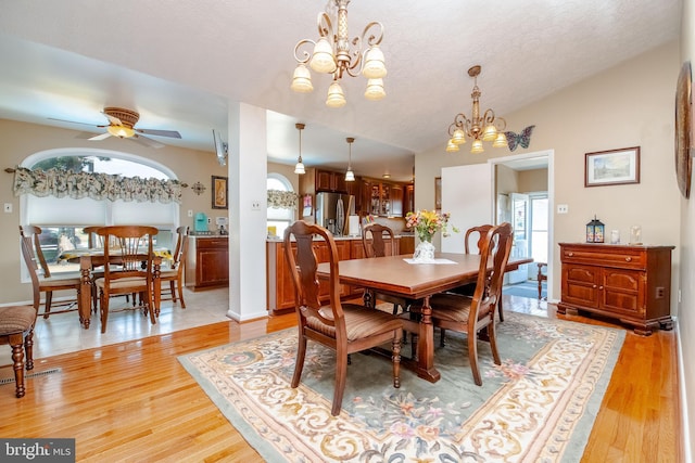 dining space featuring ceiling fan with notable chandelier, light hardwood / wood-style floors, lofted ceiling, and a textured ceiling