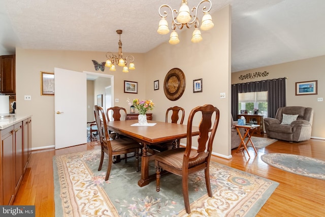 dining area with light hardwood / wood-style floors, lofted ceiling, a textured ceiling, and a chandelier