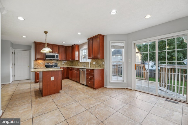 kitchen with pendant lighting, a center island, appliances with stainless steel finishes, and light stone countertops