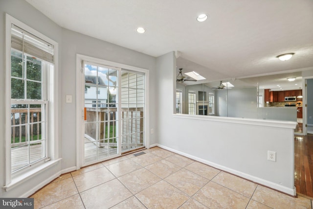 unfurnished dining area featuring light tile patterned flooring, ceiling fan, and a skylight