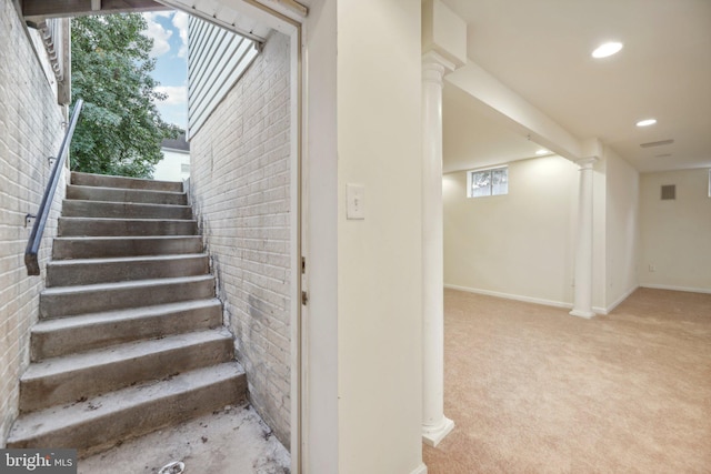 stairway with decorative columns, brick wall, and carpet floors