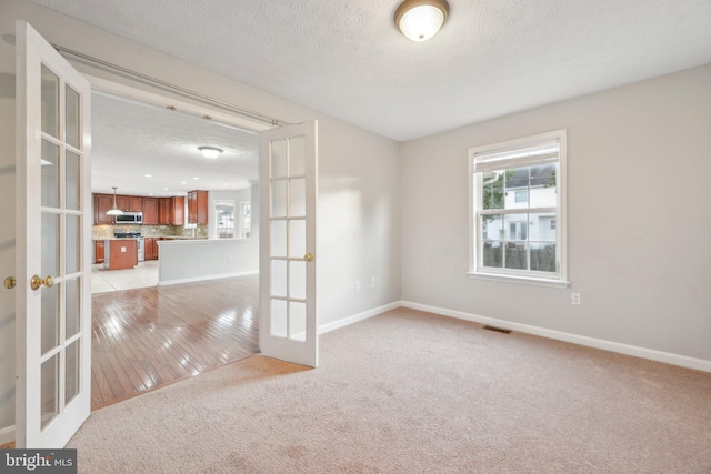 unfurnished room with french doors, light carpet, and a textured ceiling