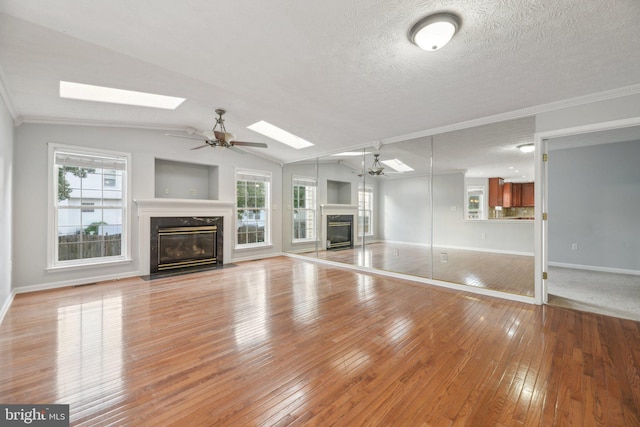 unfurnished living room featuring a wealth of natural light, a fireplace, vaulted ceiling with skylight, and light wood-type flooring