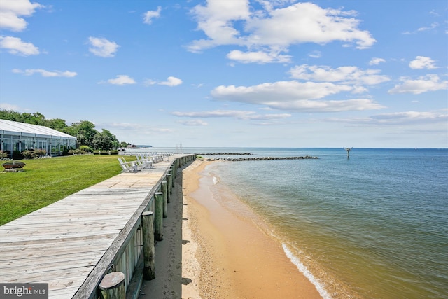 dock area with a beach view, a yard, and a water view