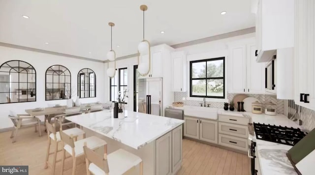 kitchen with white cabinetry, sink, a center island, a kitchen breakfast bar, and pendant lighting