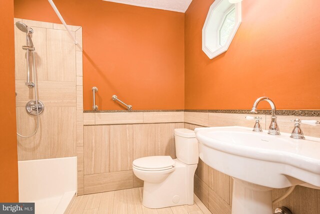 bathroom featuring a tile shower, sink, a textured ceiling, toilet, and tile walls