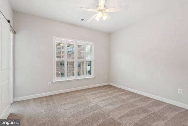 carpeted spare room with ceiling fan and a barn door