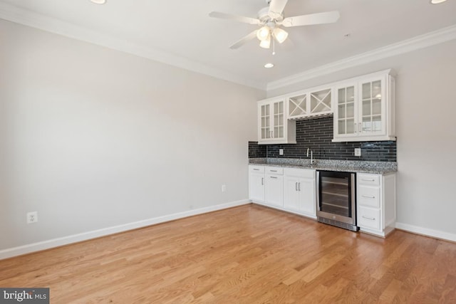 kitchen with wine cooler, sink, crown molding, white cabinets, and light stone counters