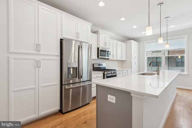 kitchen with decorative light fixtures, white cabinetry, stainless steel appliances, an island with sink, and sink