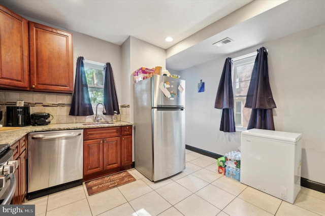 kitchen featuring decorative backsplash, light stone counters, stainless steel appliances, sink, and light tile patterned flooring