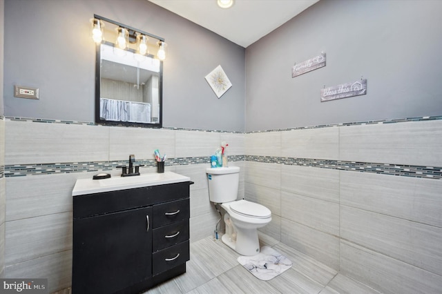 bathroom with tile patterned floors, walk in shower, vanity, tile walls, and toilet