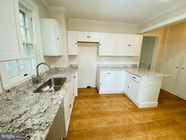 kitchen with sink, light stone counters, light wood-type flooring, white cabinets, and ornamental molding