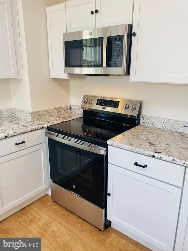 kitchen with white cabinetry, stainless steel appliances, light stone counters, and light hardwood / wood-style flooring