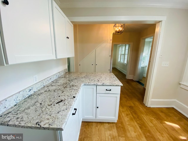 kitchen featuring pendant lighting, white cabinets, light hardwood / wood-style flooring, light stone counters, and a chandelier