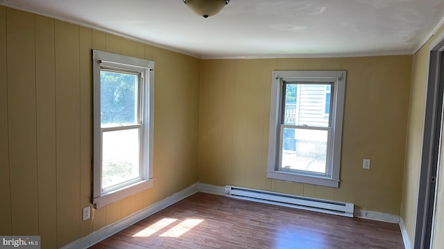 empty room with hardwood / wood-style flooring, a wealth of natural light, a baseboard heating unit, and wood walls