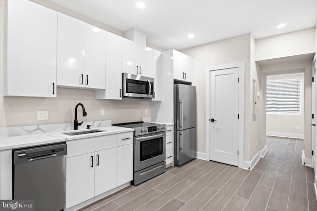 kitchen with wood tiled floor, recessed lighting, appliances with stainless steel finishes, white cabinets, and a sink