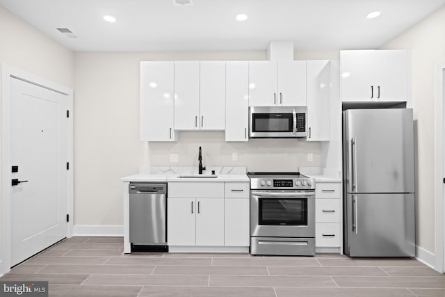 kitchen with wood tiled floor, light countertops, stainless steel appliances, white cabinetry, and a sink