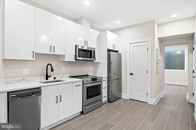 kitchen featuring a sink, recessed lighting, appliances with stainless steel finishes, white cabinets, and wood tiled floor