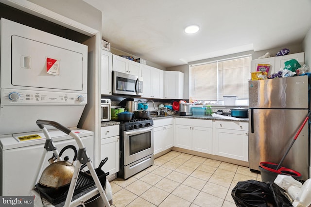 kitchen featuring stacked washer and clothes dryer, dark stone countertops, appliances with stainless steel finishes, light tile patterned flooring, and white cabinetry