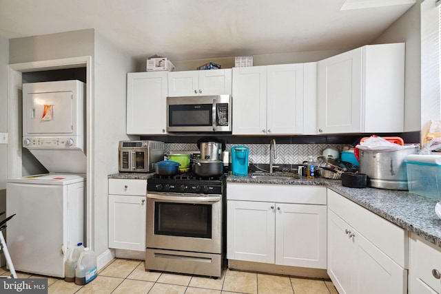 kitchen with stacked washing maching and dryer, stainless steel appliances, white cabinetry, and sink