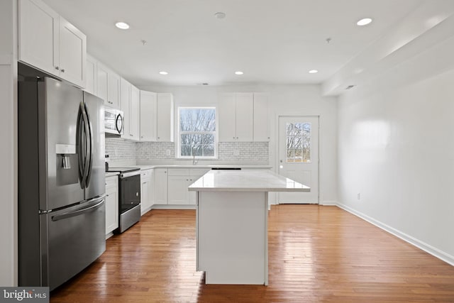 kitchen featuring decorative backsplash, stainless steel appliances, sink, a center island, and white cabinetry