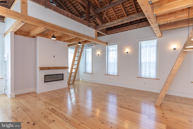 unfurnished living room with light hardwood / wood-style flooring, beamed ceiling, wooden ceiling, and a high ceiling