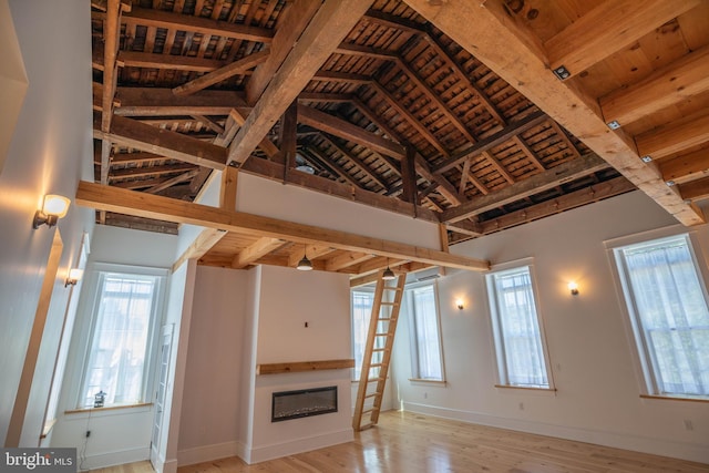 unfurnished living room with a towering ceiling, beamed ceiling, wooden ceiling, and light wood-type flooring