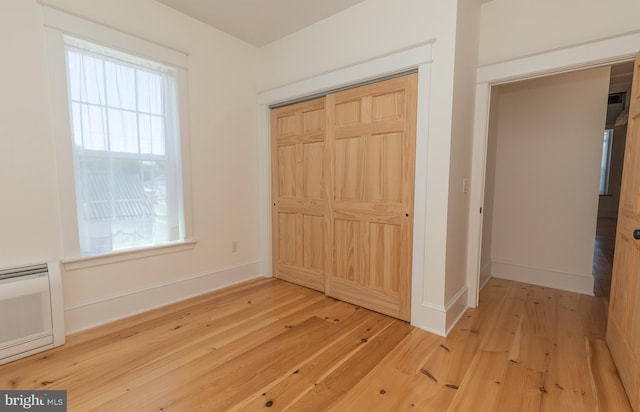 unfurnished bedroom with hardwood / wood-style floors, a wall unit AC, and a closet