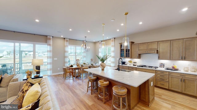 kitchen featuring hanging light fixtures, sink, a kitchen island with sink, and light hardwood / wood-style flooring