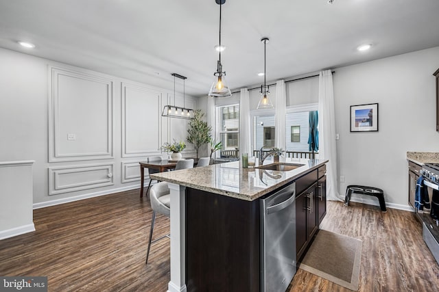 kitchen with pendant lighting, a kitchen island with sink, dark wood-type flooring, sink, and appliances with stainless steel finishes