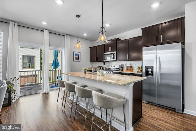 kitchen with dark brown cabinetry, light stone countertops, dark wood-type flooring, stainless steel appliances, and decorative light fixtures