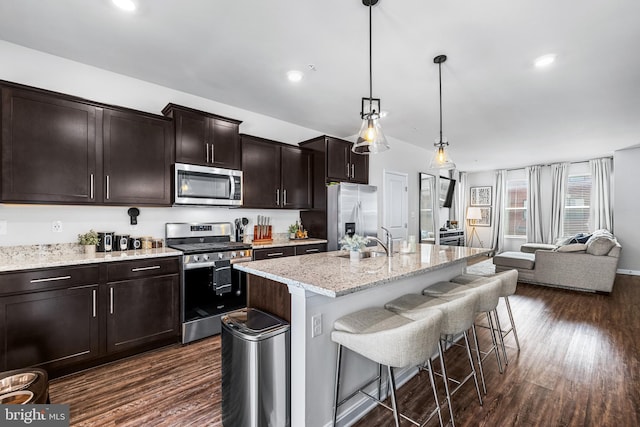 kitchen featuring a kitchen breakfast bar, stainless steel appliances, pendant lighting, a center island with sink, and dark hardwood / wood-style floors