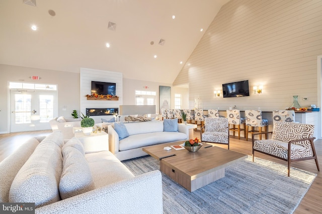 living room with a large fireplace, light hardwood / wood-style floors, and high vaulted ceiling