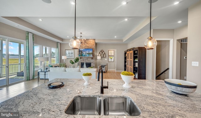 kitchen featuring hardwood / wood-style flooring, a stone fireplace, light stone counters, and sink