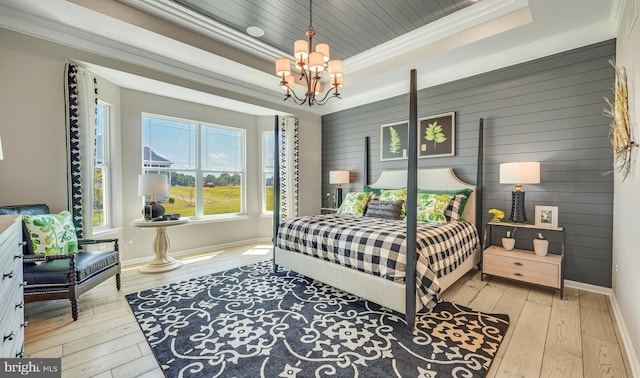 bedroom featuring wood walls, a raised ceiling, ornamental molding, a notable chandelier, and light hardwood / wood-style floors