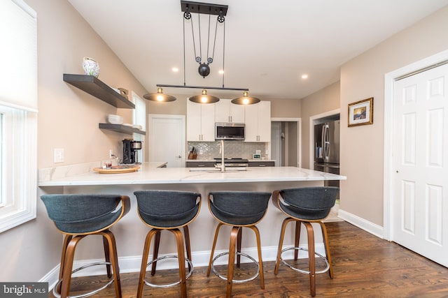 kitchen with dark wood-type flooring, pendant lighting, decorative backsplash, white cabinets, and appliances with stainless steel finishes