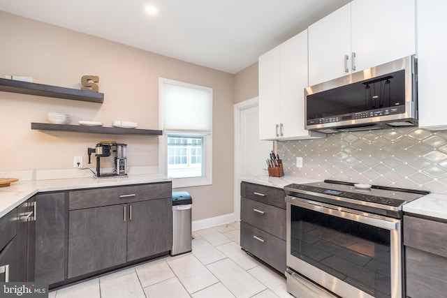 kitchen featuring light stone countertops, decorative backsplash, dark brown cabinets, white cabinets, and appliances with stainless steel finishes