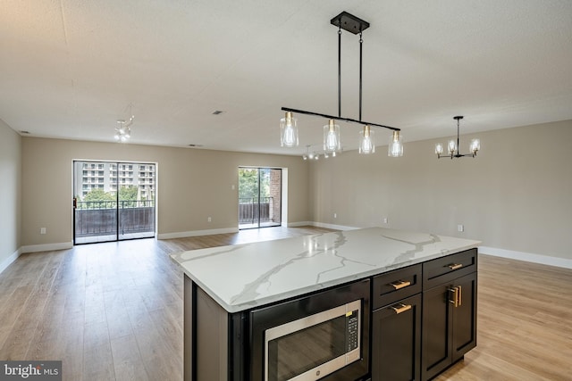 kitchen with a center island, stainless steel microwave, hanging light fixtures, light wood-type flooring, and light stone counters