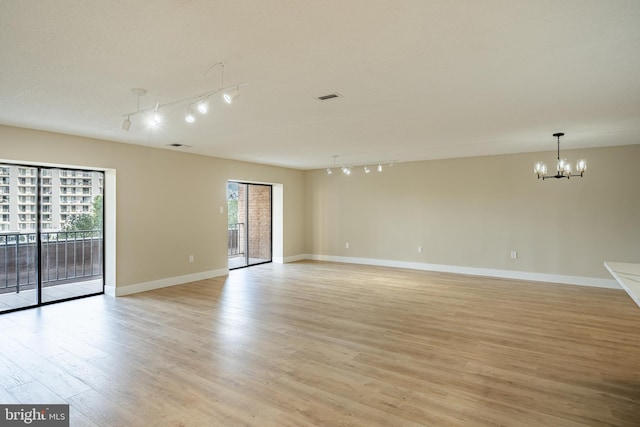 empty room featuring an inviting chandelier, a healthy amount of sunlight, track lighting, and light wood-type flooring