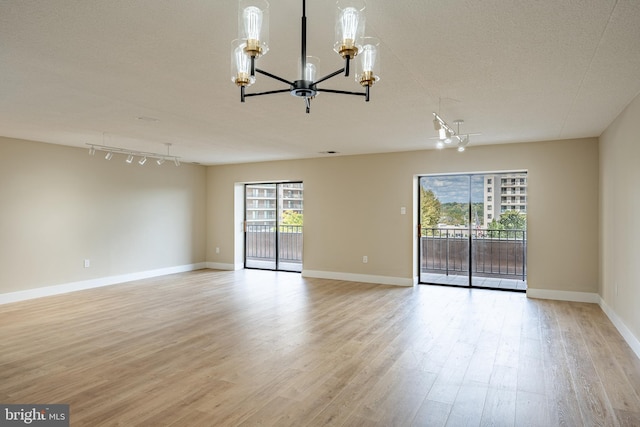 empty room featuring rail lighting, light hardwood / wood-style floors, a textured ceiling, and a notable chandelier