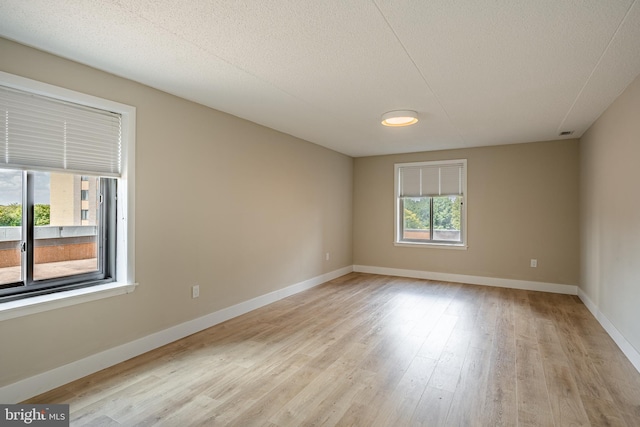 unfurnished room with light wood-type flooring and a textured ceiling