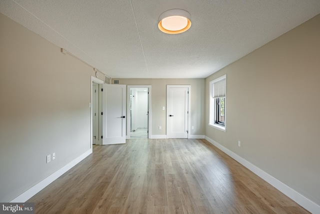 empty room with a textured ceiling and light hardwood / wood-style flooring