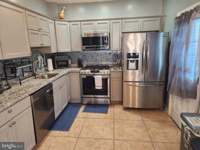 kitchen with sink, decorative backsplash, light tile patterned flooring, light stone counters, and stainless steel appliances