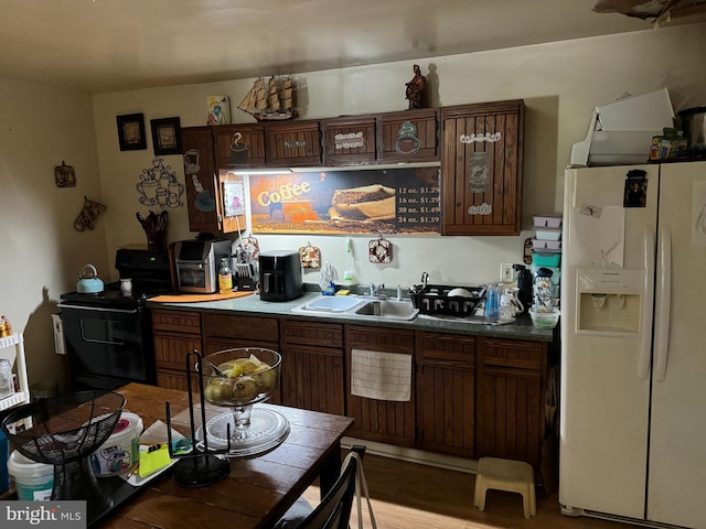 kitchen featuring dark brown cabinetry, black stove, sink, white refrigerator with ice dispenser, and light wood-type flooring