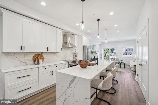 kitchen with dark hardwood / wood-style floors, an island with sink, wall chimney range hood, and stainless steel appliances