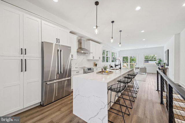 kitchen featuring a kitchen island with sink, wall chimney exhaust hood, light wood-type flooring, and stainless steel appliances