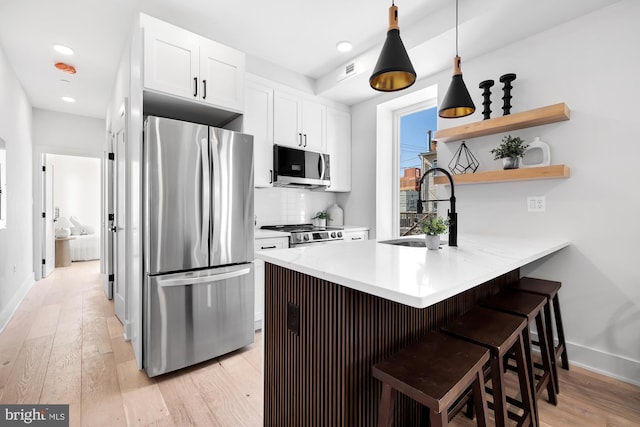 kitchen featuring sink, kitchen peninsula, a breakfast bar area, white cabinetry, and stainless steel appliances