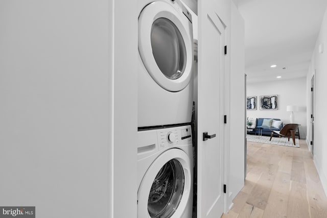 clothes washing area with stacked washer / drying machine and light wood-type flooring