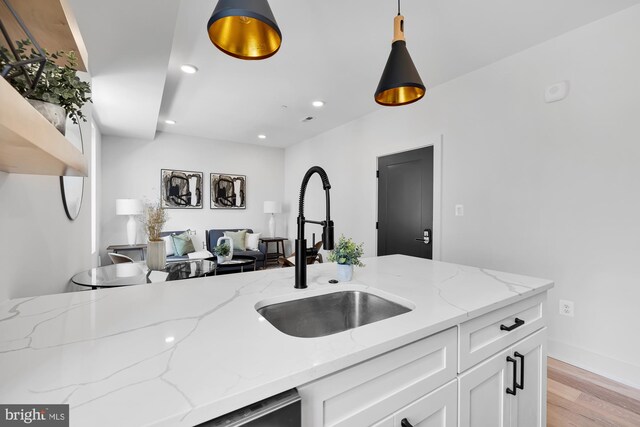 kitchen with sink, light stone counters, light hardwood / wood-style floors, decorative light fixtures, and white cabinets